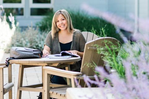 Indigenous female business student studying outdoors at a wooden table.