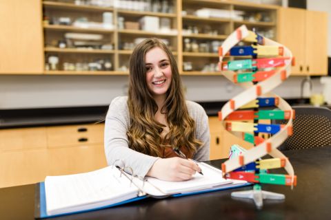 Science student studies with her books close to a model of DNA