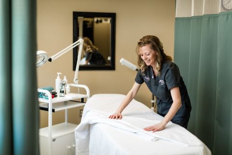 Esthetics student covers a treatment bed with linens in preparation for a client.