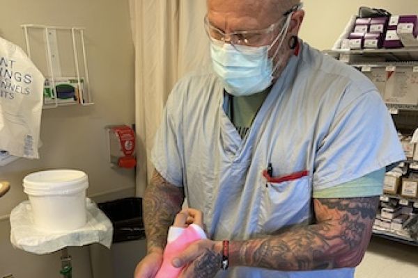 Licensed Practical Nurse Jim Fishley holding the arm of a patient with a pink cast