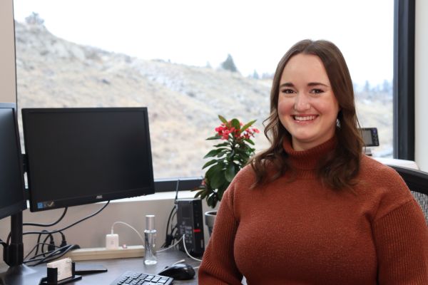 Electronics engineering alum Emily Schatz sits at a computer desk by a window overlooking the mountain